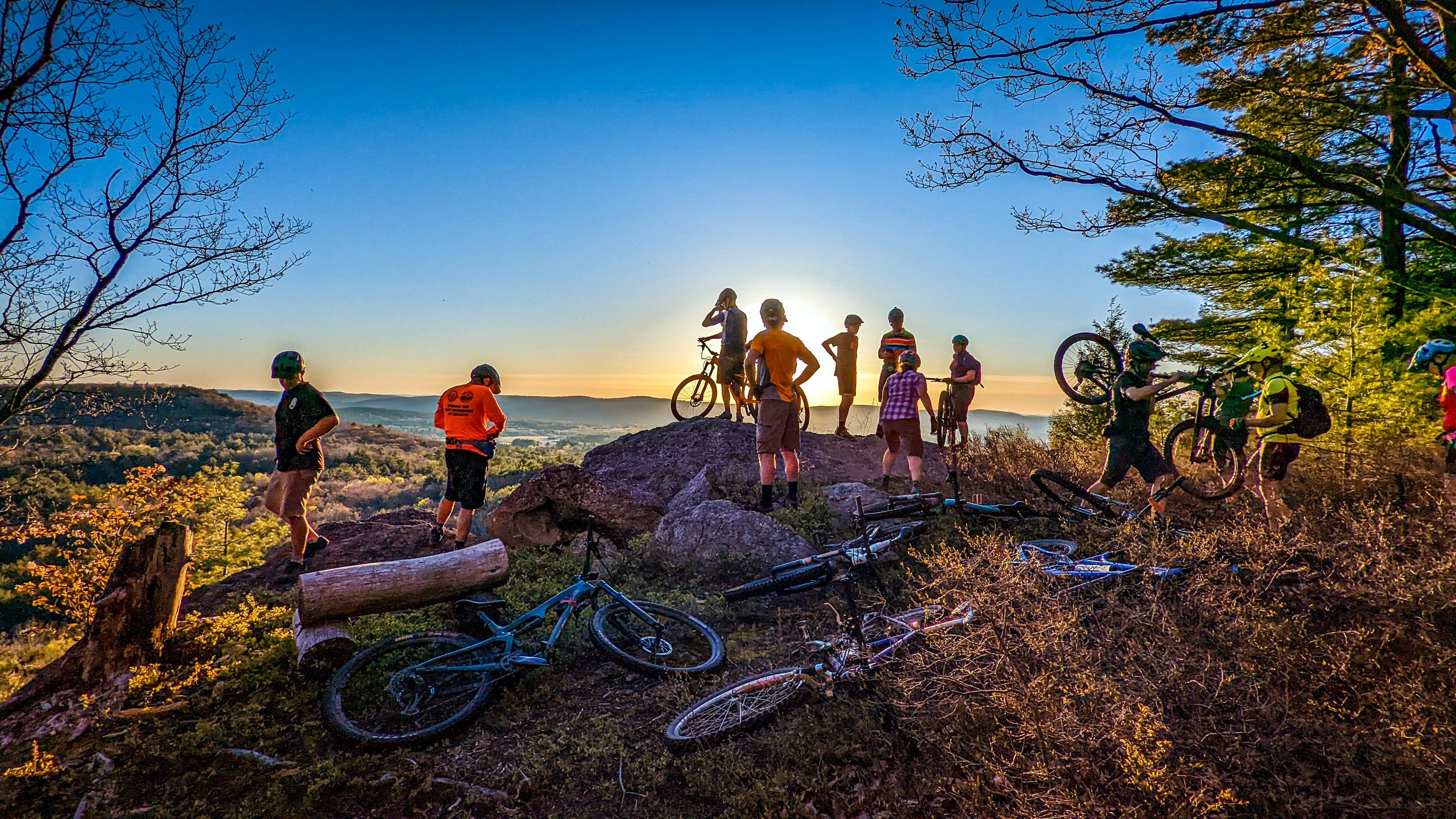 Group of cyclists standing on the edge of a large rocky hill overlooking scenic view.
