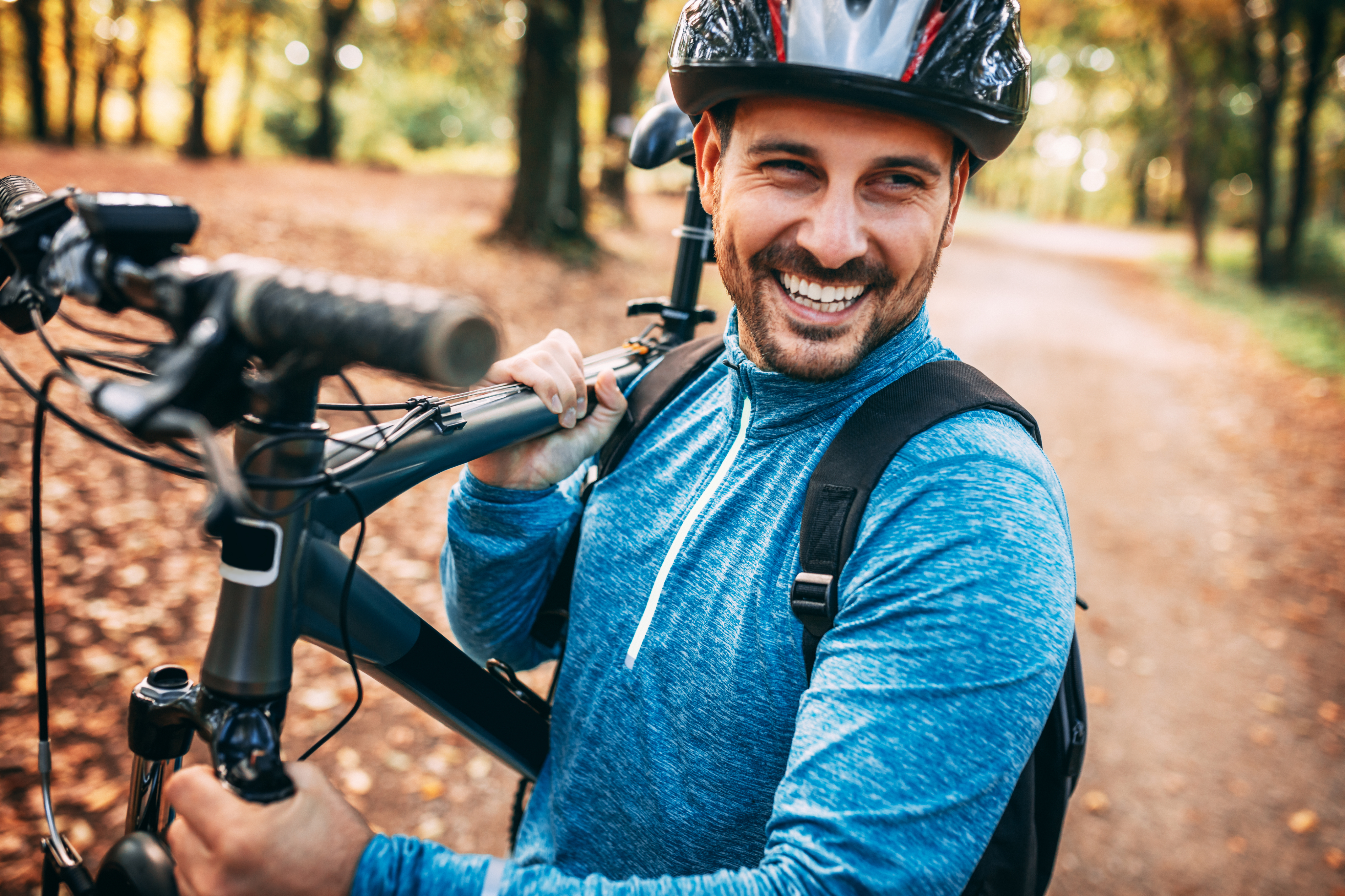 Guy wearing bicycle gear and helmet holding his mountain bike up on his shoulders while smiling.