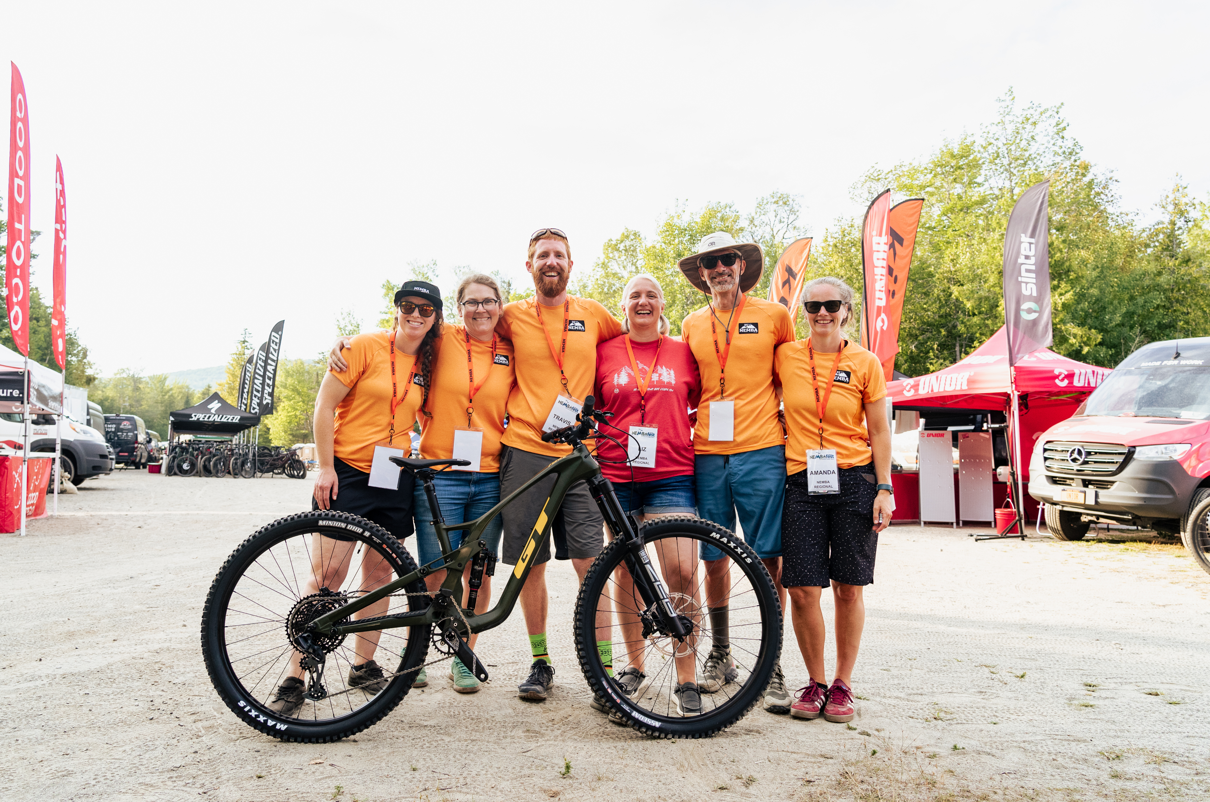 6 NEMBA Members at a NEMBA event standing and posing for a picture with a mountain bike.