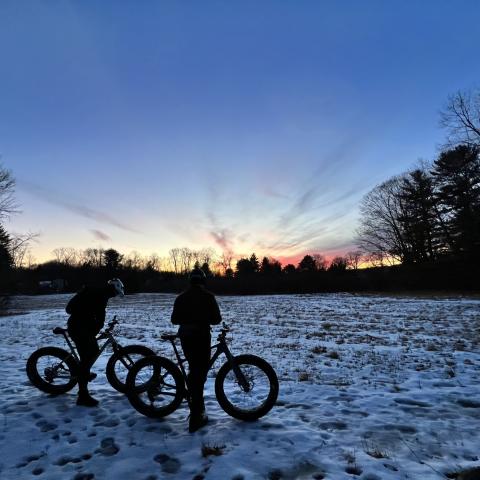 Photo of two people standing beside their bikes in a snowy field.