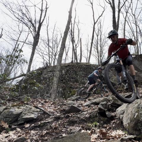 Photo of a person cycling through rough terrain in a rocky area.